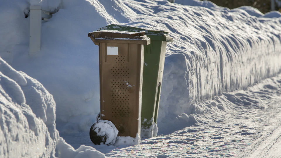 Två soptunnor vid en snötäckt väg