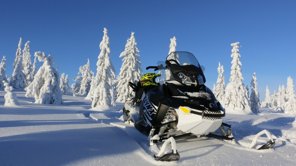 Snöskoter i solbelyst vinterlandskap.