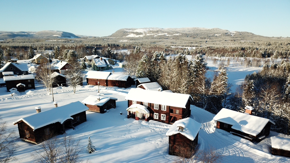 Drönarbild över snötäckta timmerhus på en gård i Hede.