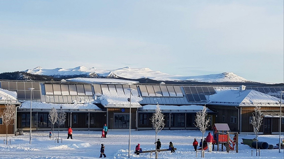 Skolbyggnad med snöklädda fjäll i bakgrunden.
