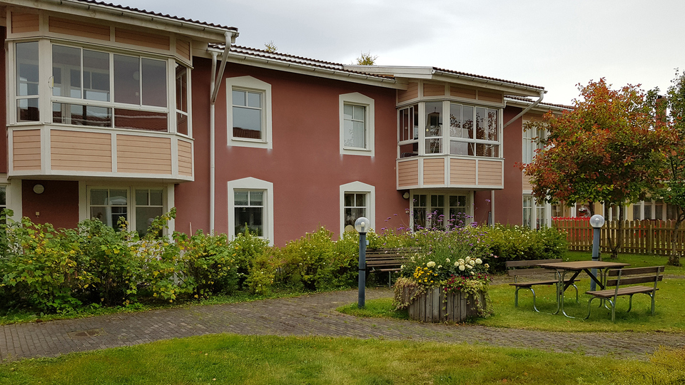 Innergård med uteplatser, lampor och blomsterarrangemang framför tvåvåningshus med balkonger och uteplats.