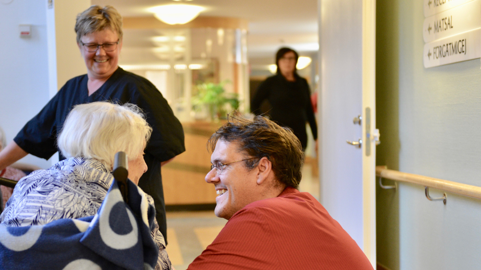 Vårdpersonal pratar med en vårdtagare i rullstol. 