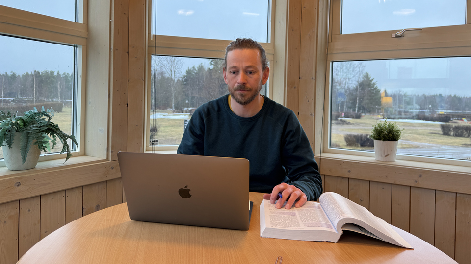 En man sitter vid ett bord framför en bärbar dator.