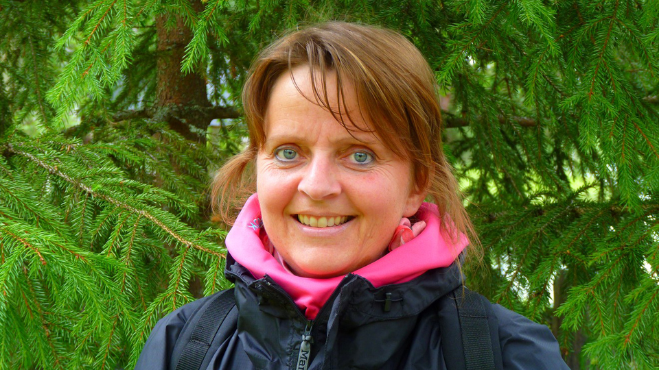 En kvinna står framför ett träd med en rosa halsduk runt halsen.