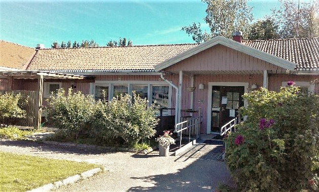 Ett rosa enplanshus med buskar vid entrén.