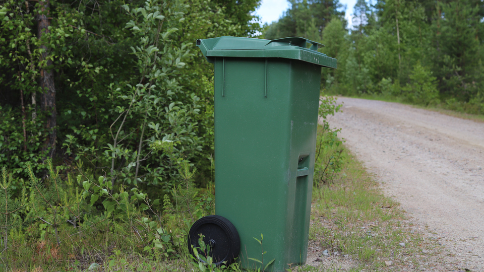 Grön soptunna vid vägkant.