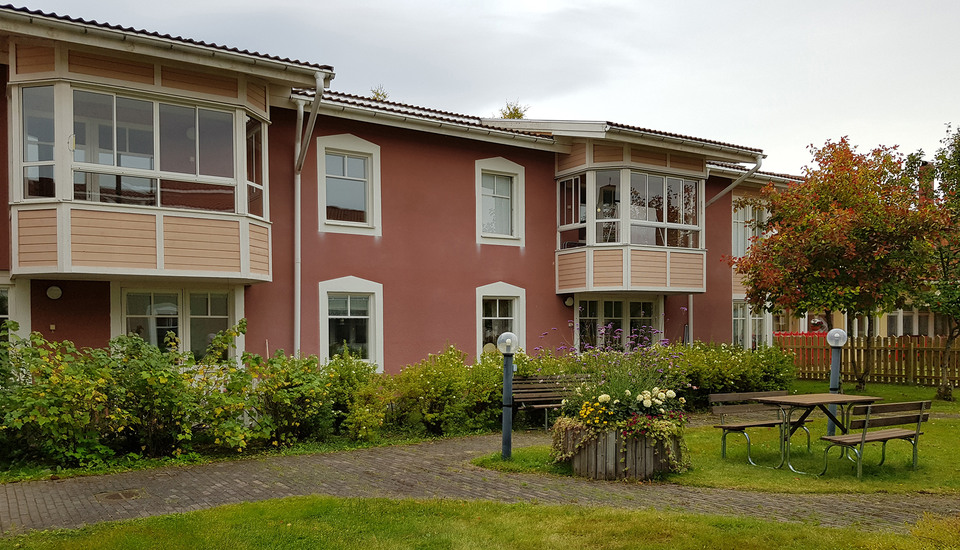 Innergård med  uteplatser, lampor och blomsterarrangemang framför tvåvåningshus med balkonger och uteplats.