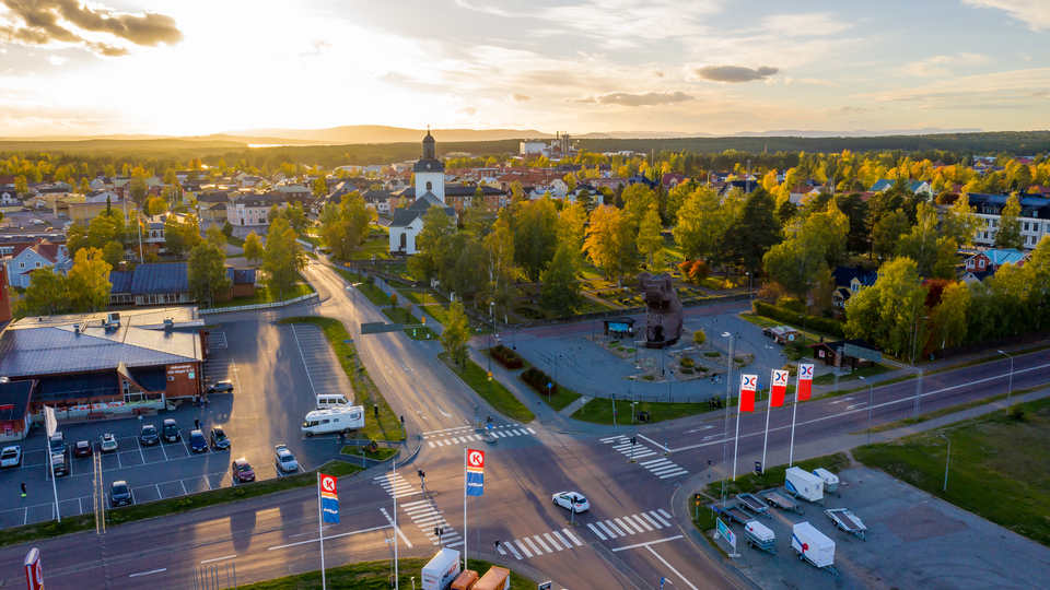 Drönarfoto över fyrvägskorsning och träbjörn. I fonden byggnader, kyrka och växtlighet i Sveg sommartid.