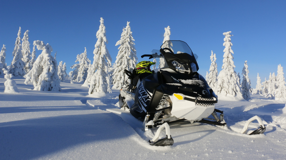Snöskoter i solbelyst vinterlandskap.