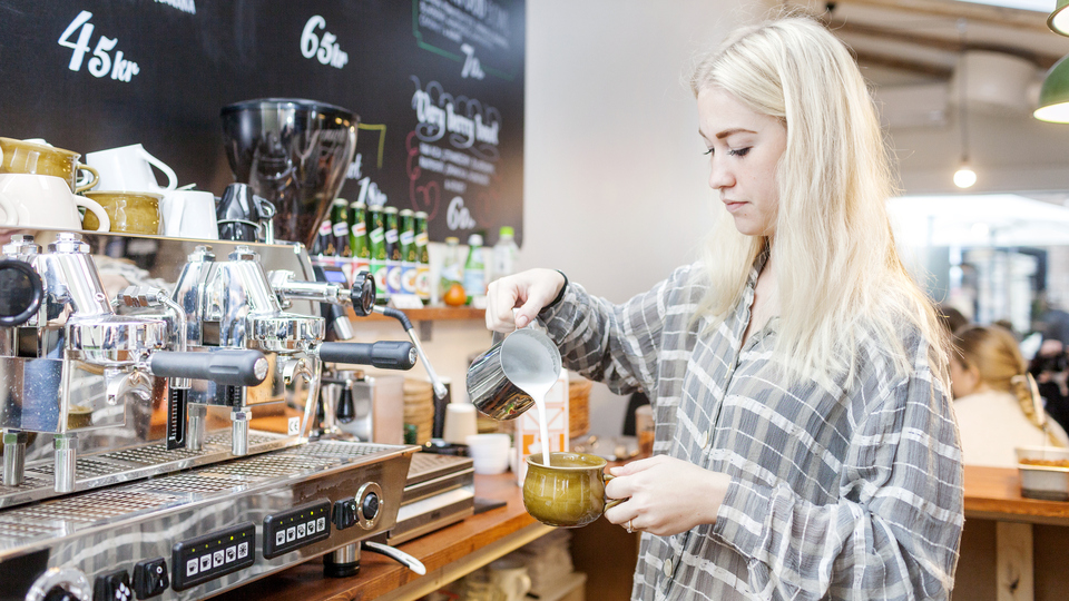En tjej häller upp en kopp kaffe på ett kafé.