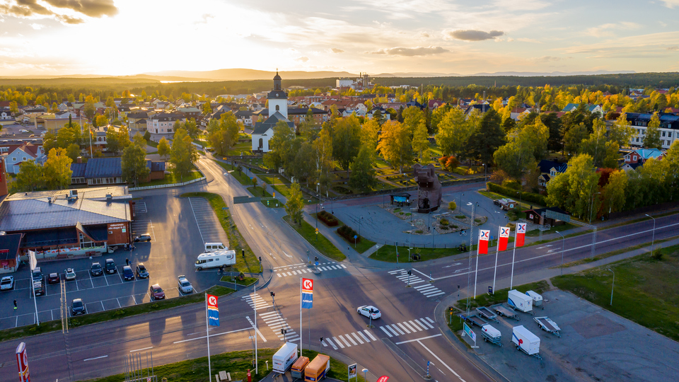 Drönarfoto över fyrvägskorsning och träbjörn. I fonden byggnader, kyrka och växtlighet i Sveg sommartid.