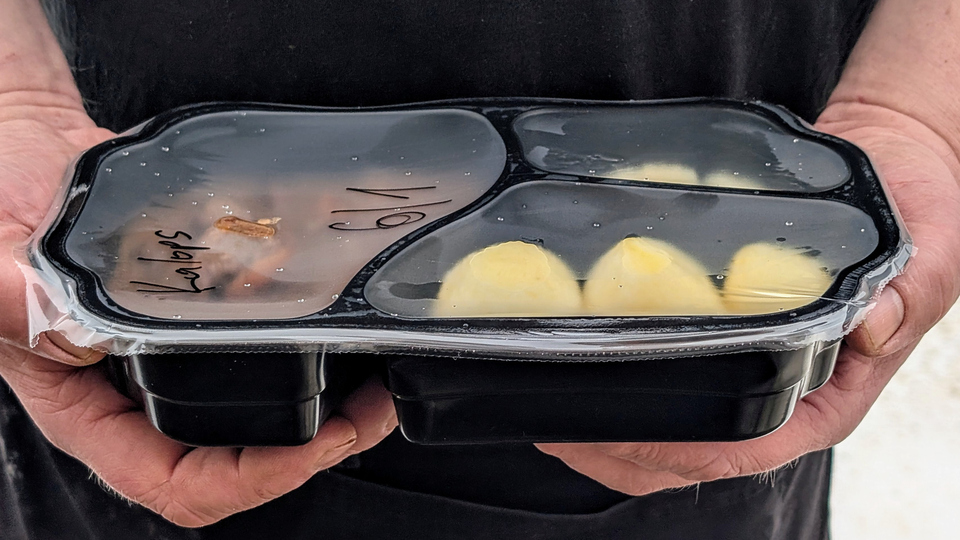 Två händer håller i en matlåda med potatis och kött