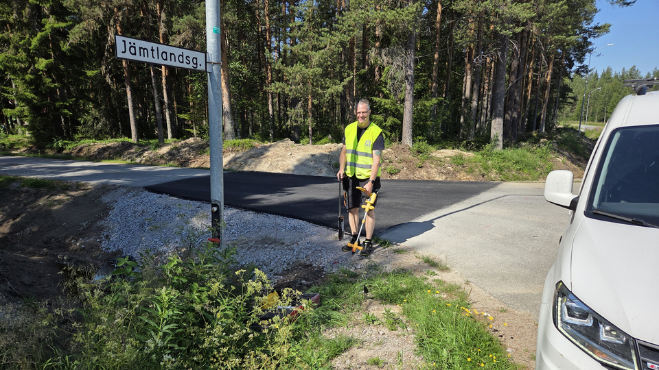 En man i gul väst står på en väg bredvid en gatuskylt.