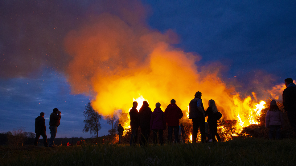 Kvällsbild med en majbrasa med publik.