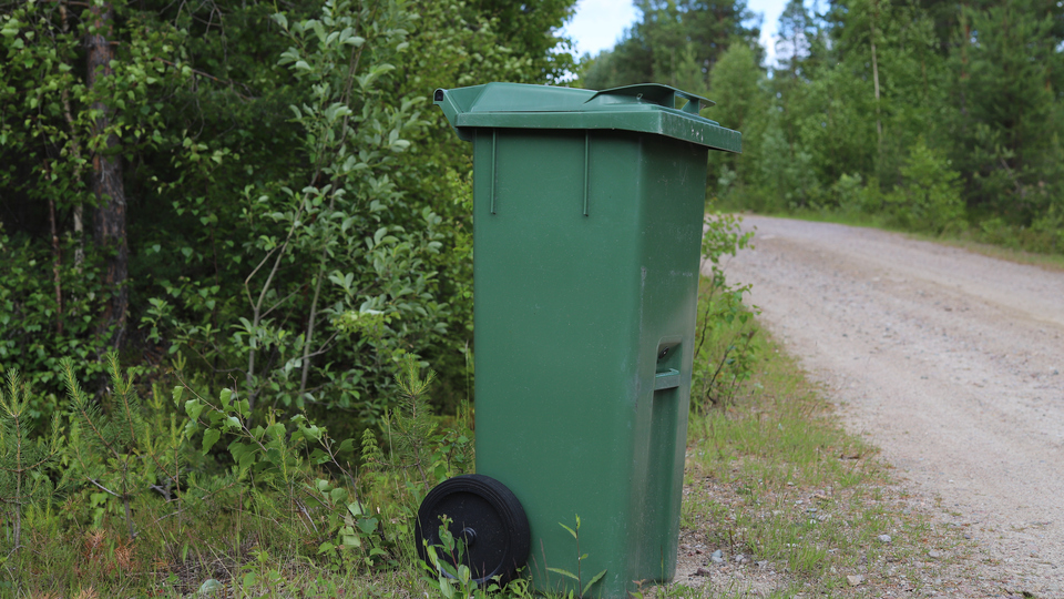 Grön soptunna vid vägkant.