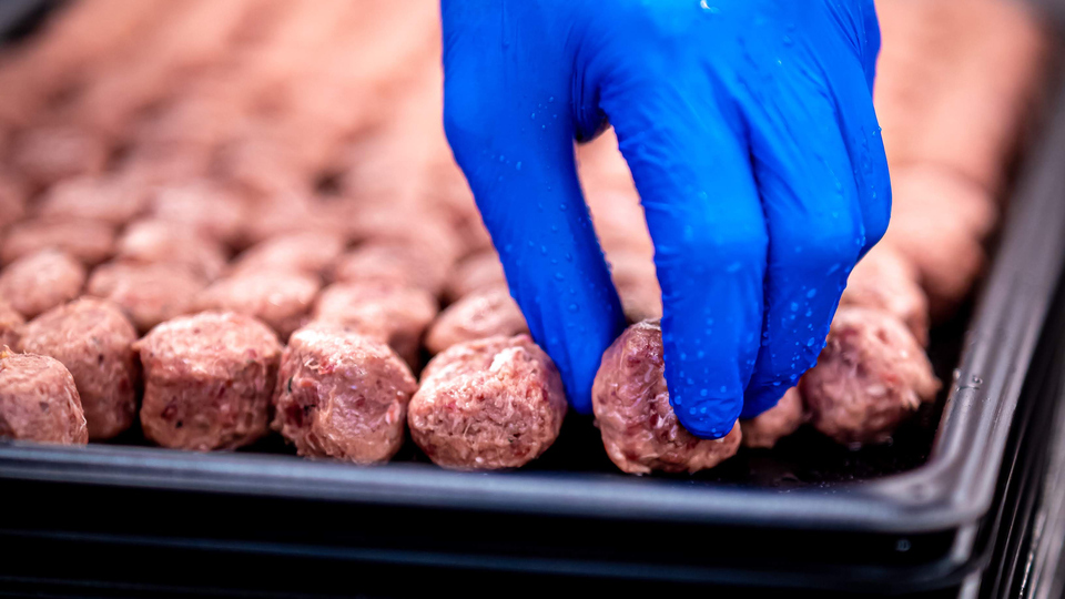 En hand med handske lägger råa köttbullar på en plåt.