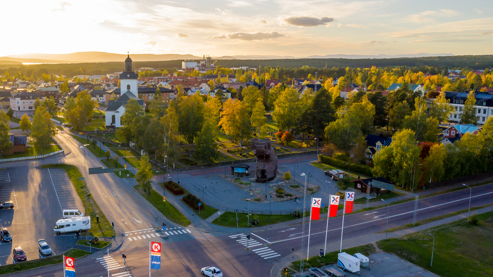 Drönarfoto över fyrvägskorsning och träbjörn. I fonden byggnader, kyrka och växtlighet i Sveg sommartid.