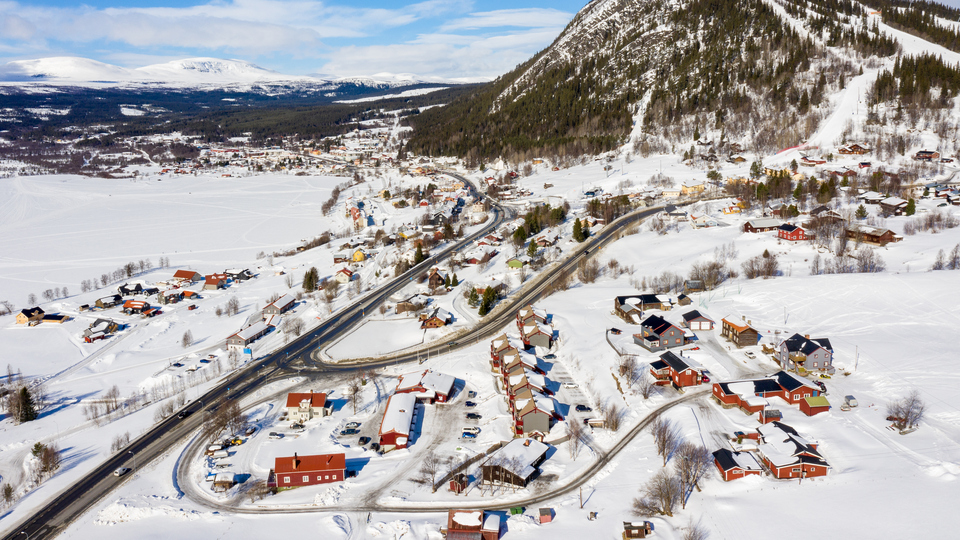Drönarbild över Funäsdalen med Funäsdalsberget i fonden. Villor och vägar mellan snötäckt sjö och skogsklätt berg med snötäckta backar.