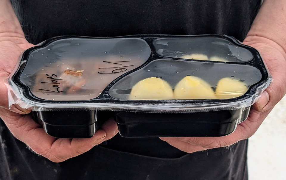 Två händer håller i en matlåda med potatis och kött