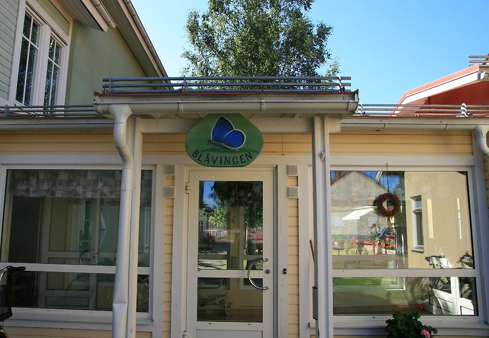 Entrédörr i glas. Ovanför dörren en skylt med en fjäril på och texten Blåvingen.