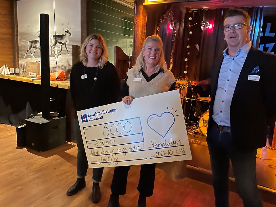 Tre personer på en scen, damen i mitten håller i en stor check på 5 000 kronor.