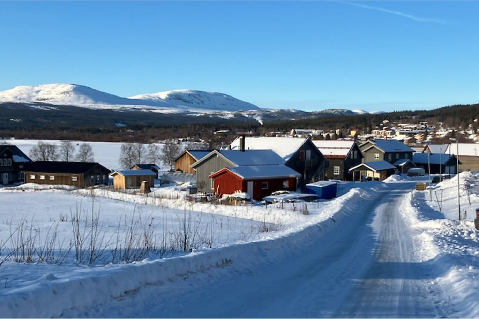 En byväg i vinterskrud med fjäll i bakgrunden.