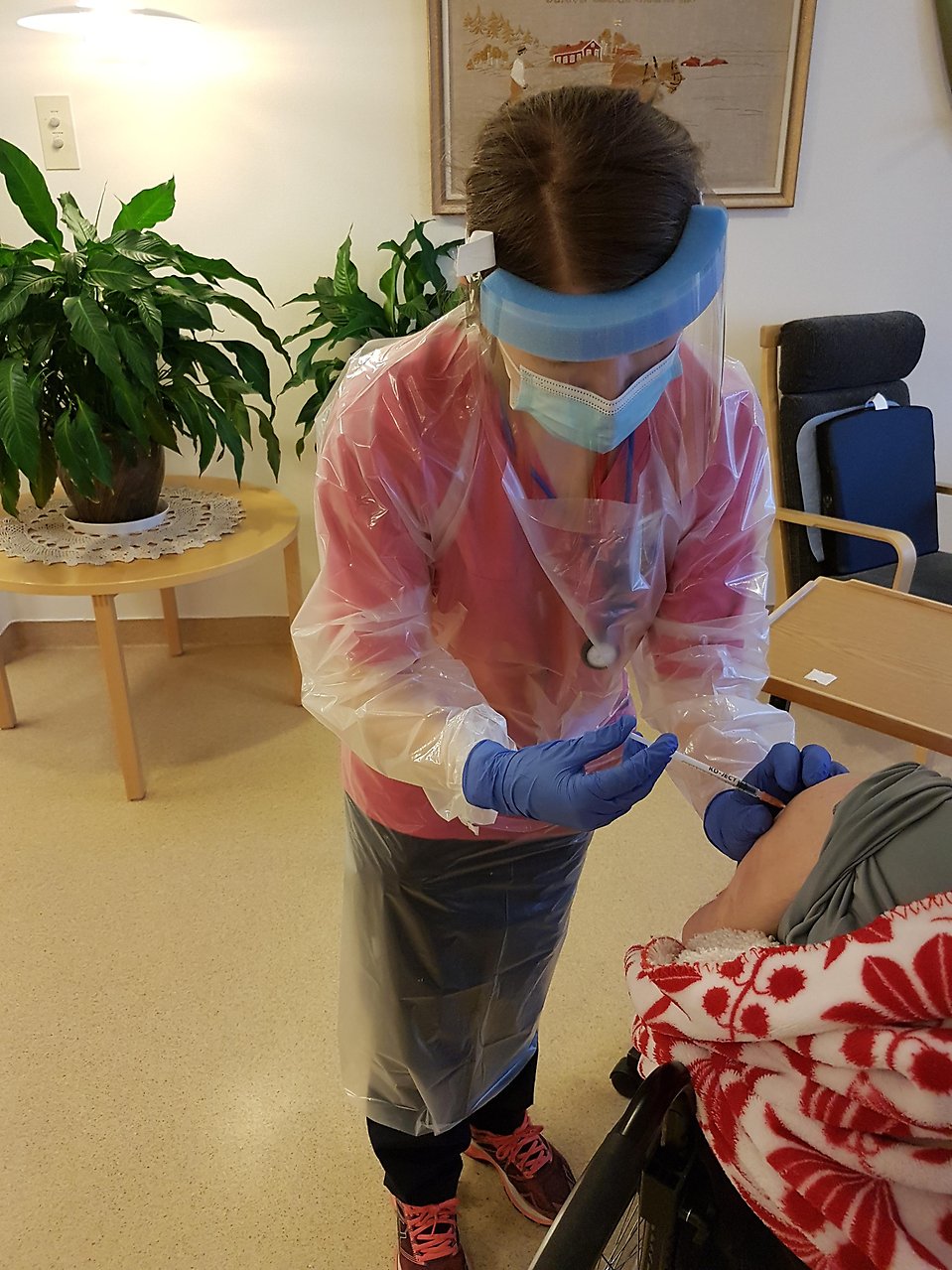 Sjuksköterska i skyddskläder vaccinerar en person som bor på särskilt boende.